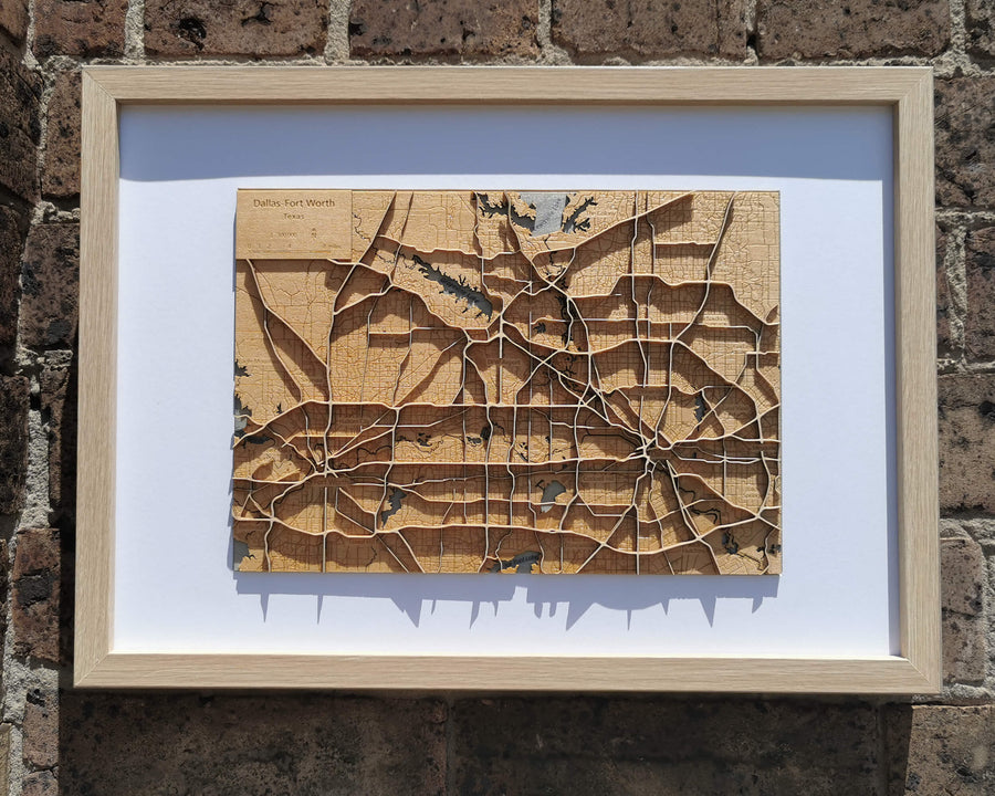 Dallas-Fort Worth wooden map art in an oak frame, hanging on a brick wall
