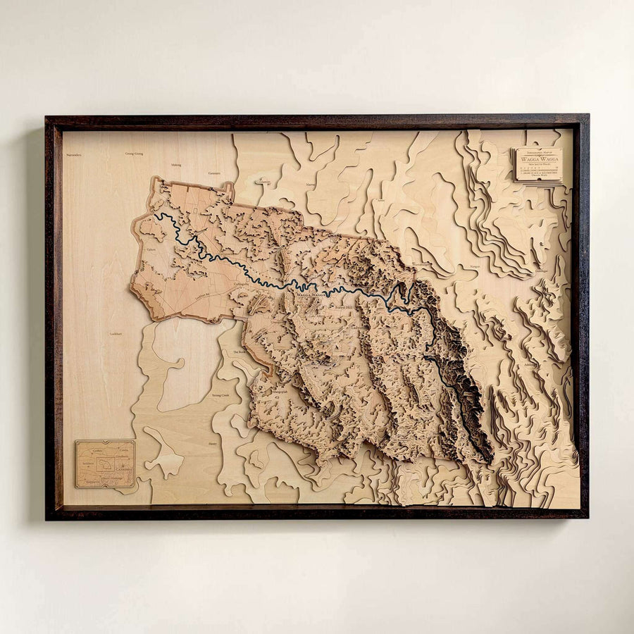 A framed 3D wooden topographic map of Wagga Wagga, NSW, showcasing raised terrain and a river with a dark wood frame, mounted on a light beige wall.