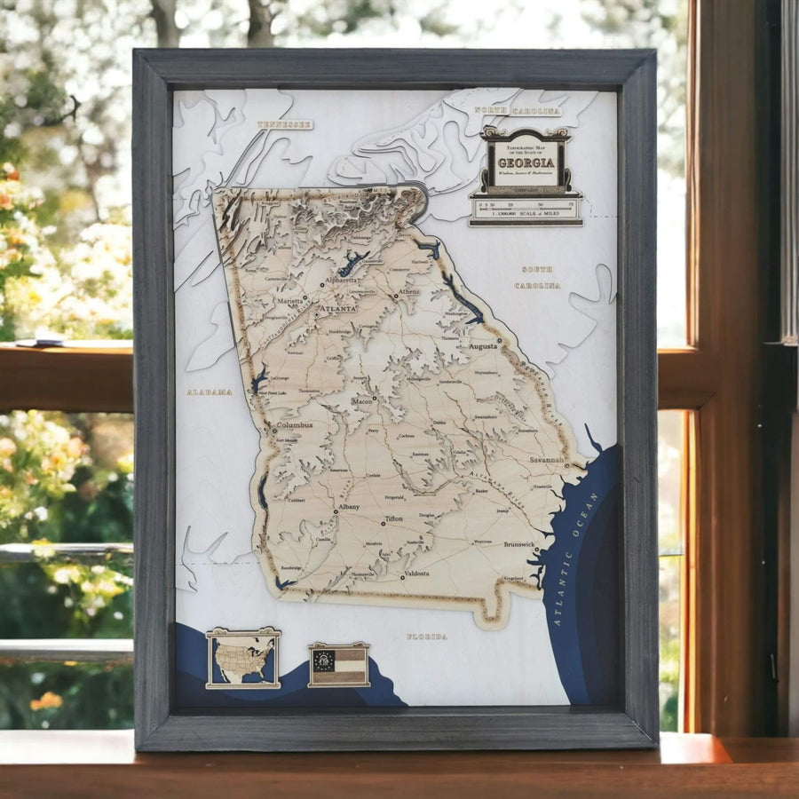 A wooden 3d carved map of the state of Georgia sits on a sun filled window sill.