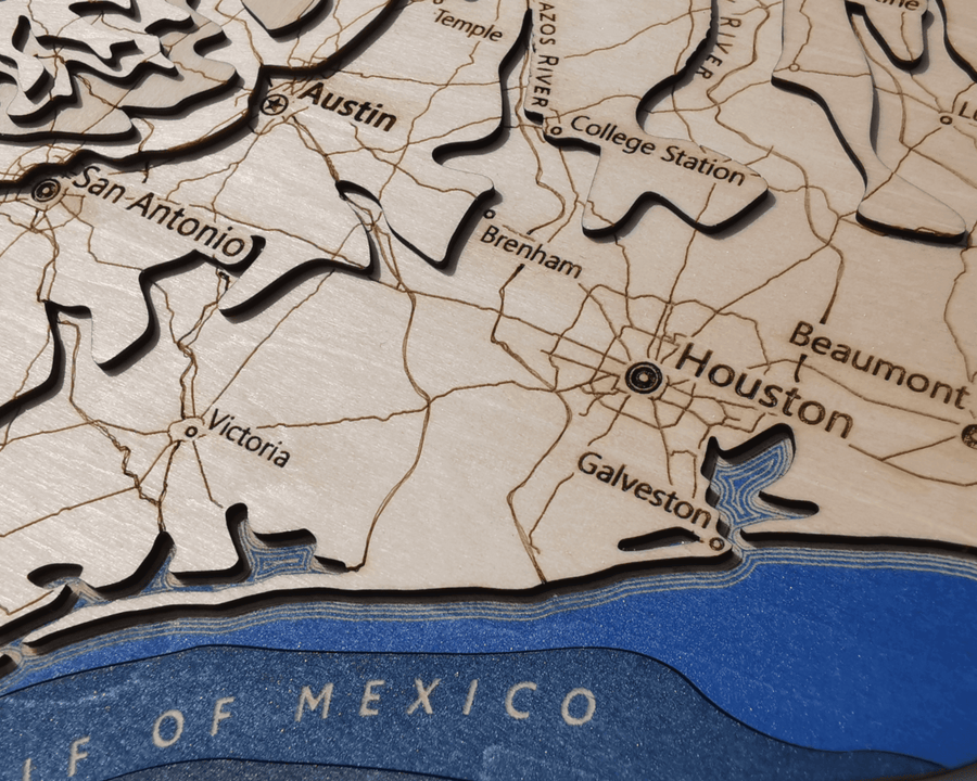 Close up of a wooden contour map of texas featuring houston, san antonio and austin
