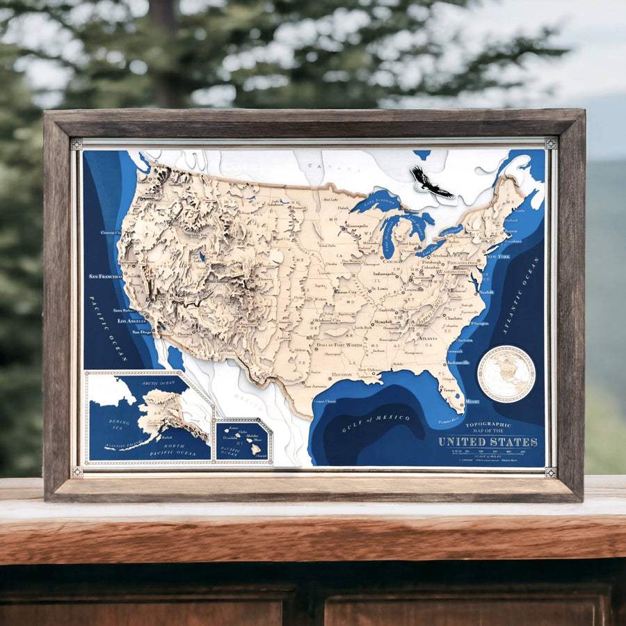 3D wooden contour map of the USA in a wooden frame sitting on a bench overlooking some pine trees